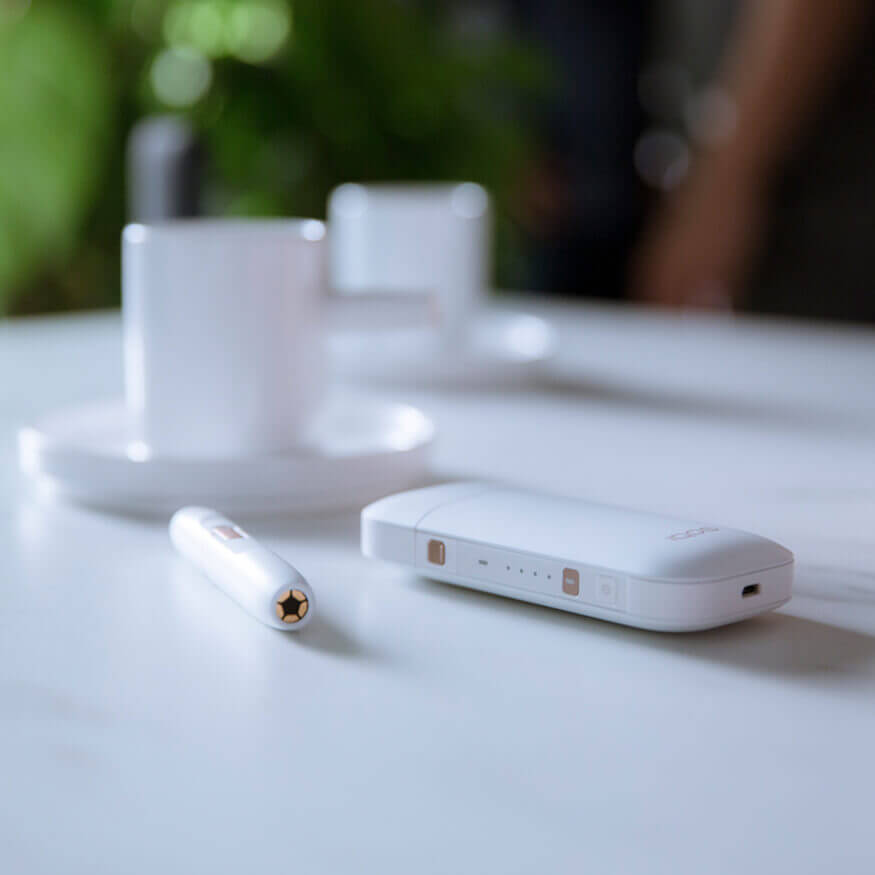 Kit IQOS 2.4 PLUS blanco en la mesa con un café