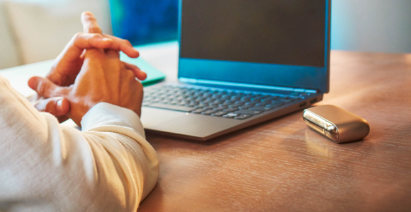 Man using his laptop with his IQOS device on the table