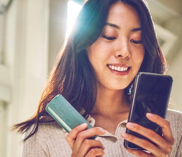 A smiling woman holding a mobile phone and IQOS device.