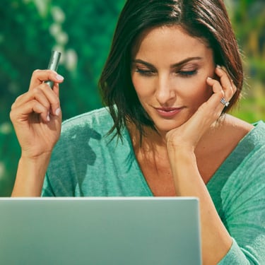 A woman holding an IQOS device while looking at a laptop screen.