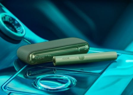 A jade green IQOS ILUMA device and charger.