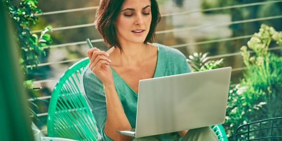 A woman holding an IQOS ILUMA device while looking at a laptop.