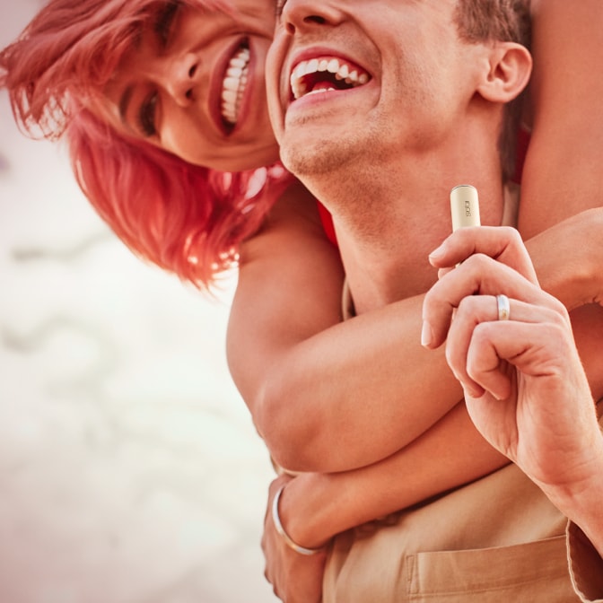 A couple embrace; he holds an IQOS ILUMA device.