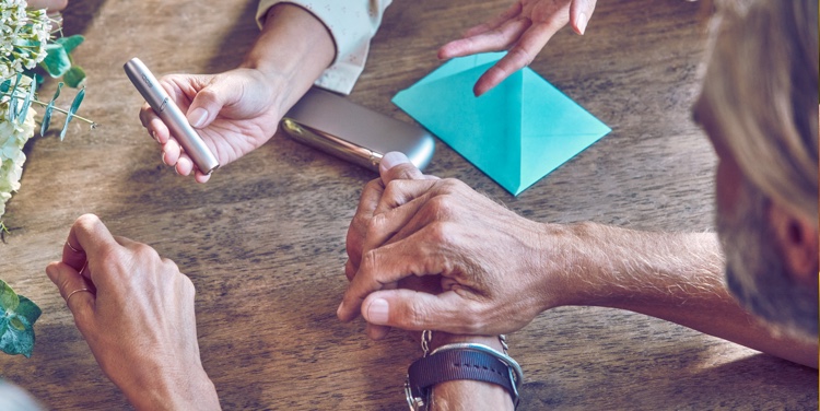 People's hands; an IQOS device in the background.