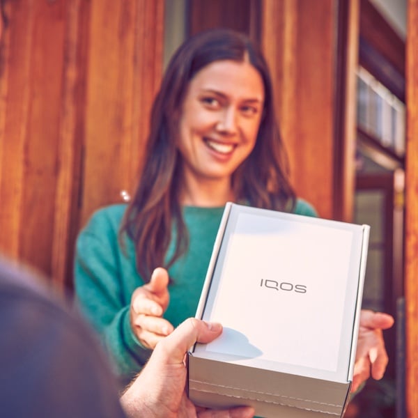 A smiling woman receives an IQOS box.