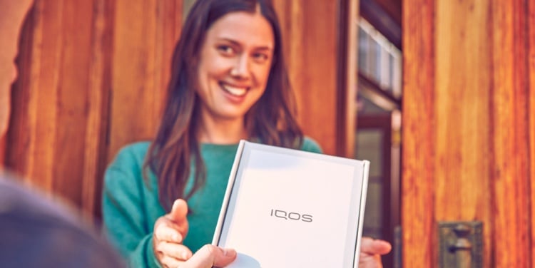 A smiling woman receives an IQOS box.
