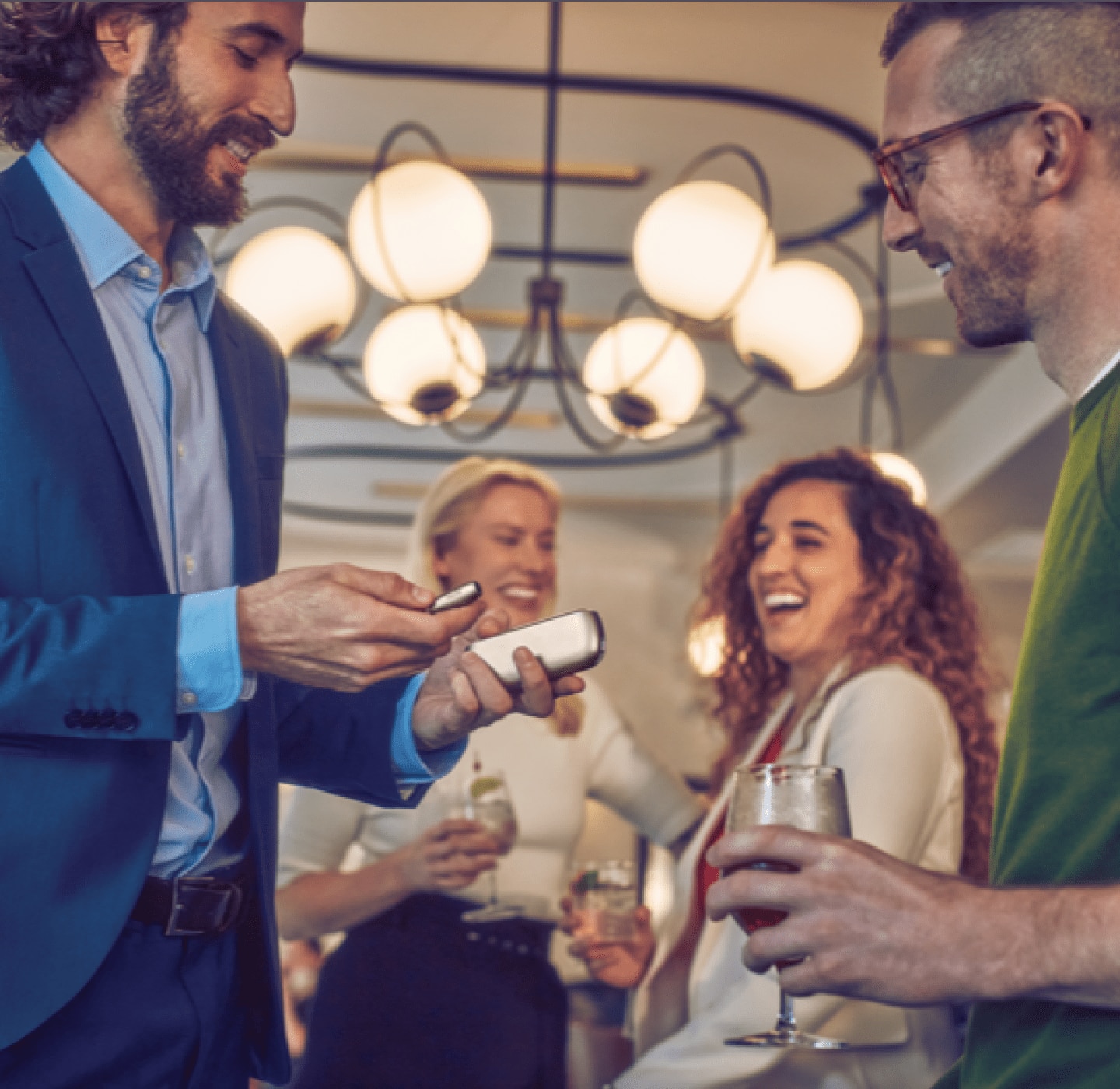 Grupo de amigos sonriendo sostienen dispositivo IQOS ILUMA Dorado comprado con descuento con un código de recomendación