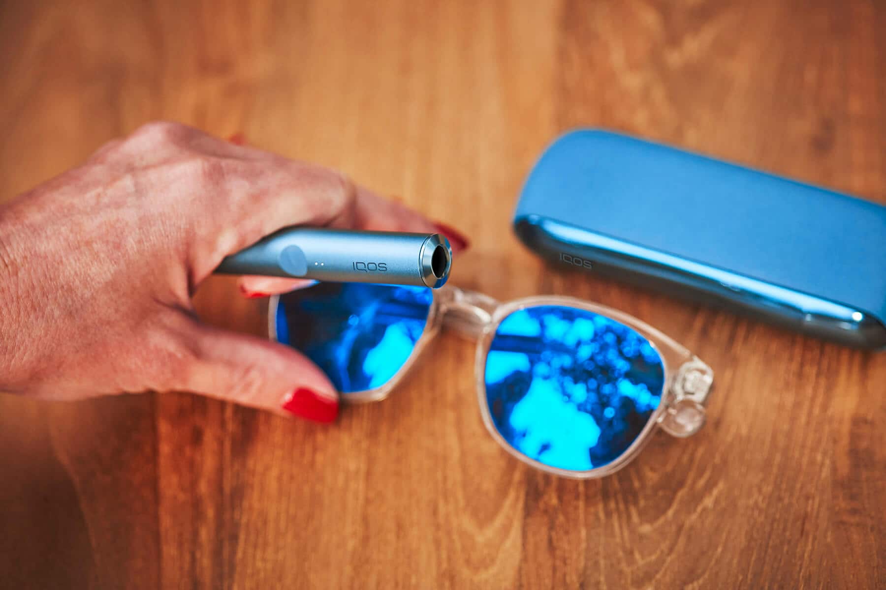 Manos con dispositivo IQOS y gafas de sol