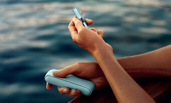 Mujer mirando al mar con dispositivo IQOS en las manos