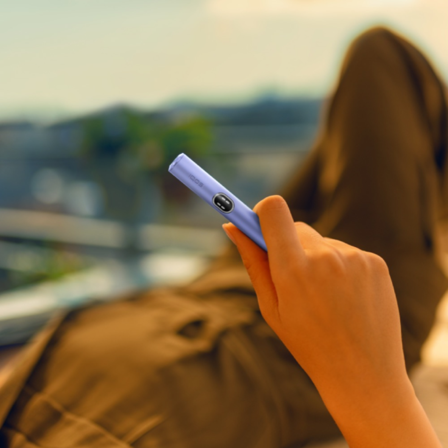 Una personsa sosteniendo un IQOS ILUMA en una terraza
