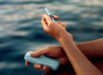 Mano sujetando cargador de bolsillo y holder de IQOS ILUMA i en Azul Brisa