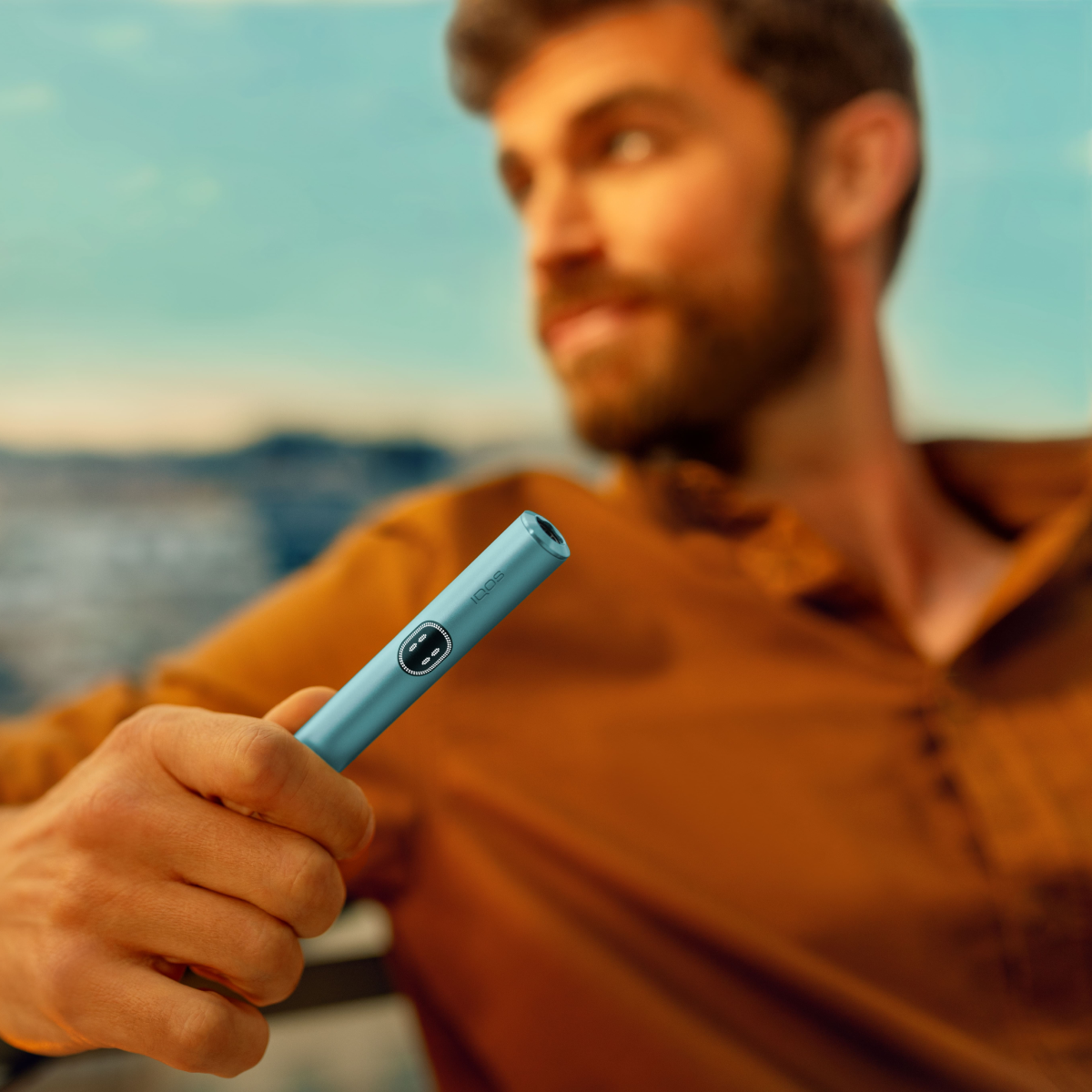 Hombre con polo naranja y barba sosteniendo un IQOS ILUMA I PRIME