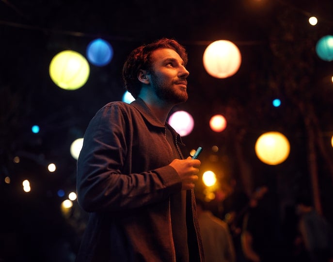 Hombre con holder de IQOS ILUMA i Azul Brisa y en el fondo luces de colores