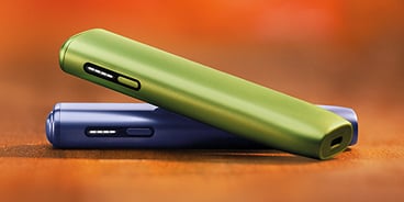 Dos dispositivos IQOS ILUMA sobre un fondo naranja