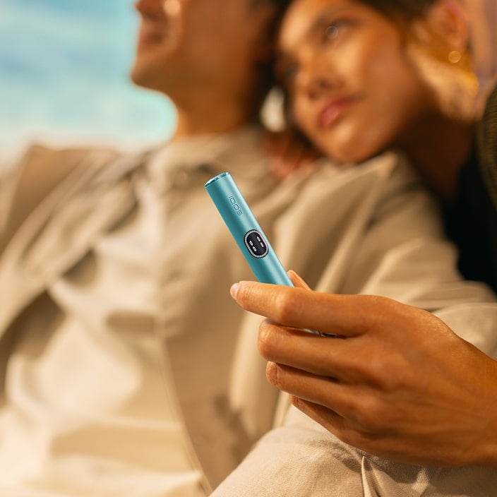 Mujer y hombre sonriendo con el holder de IQOS ILUMA i Azul Brisa en la mano