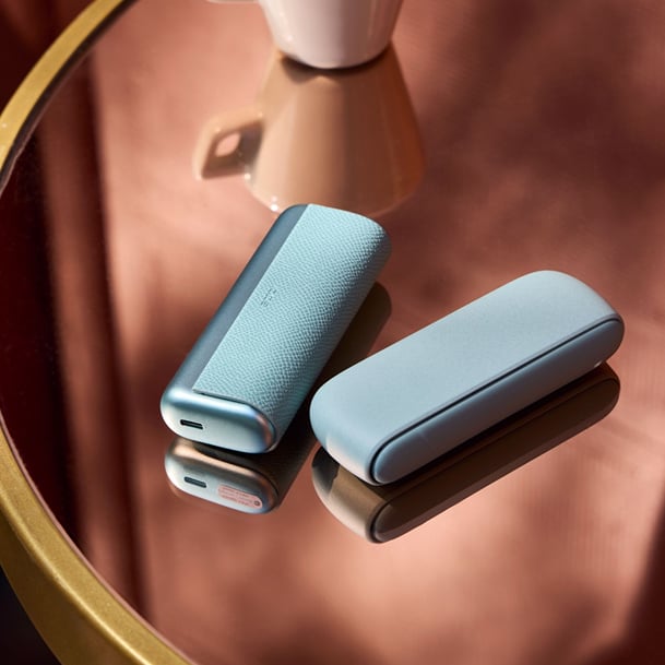 Dispositivo IQOS sobre mesa de cristal con un cafe