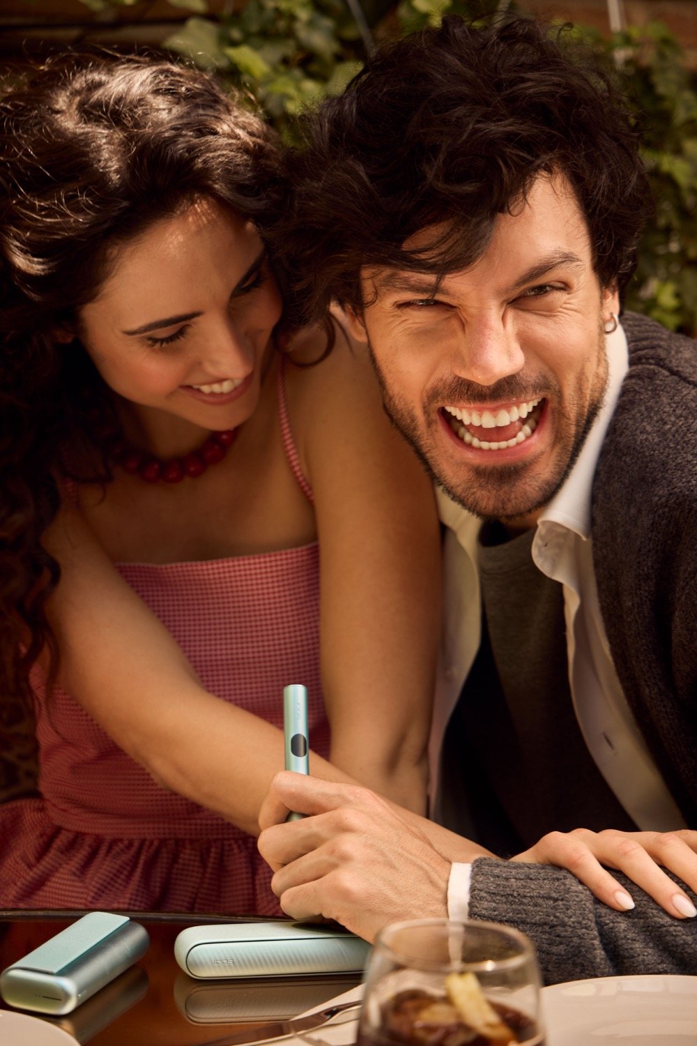 Dos personas riendose a la vez mientras una agarra un dispositivo IQOS