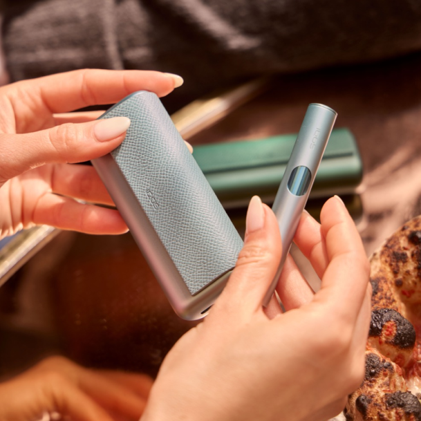 Manos sosteniendo un estuche y un dispositivo IQOS