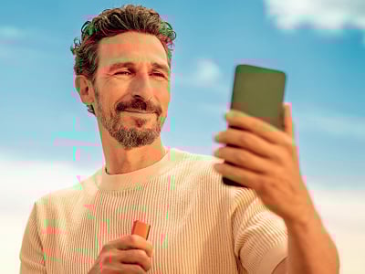 Una persona mirando su móvil en una mano y en la otro un dispositivo IQOS