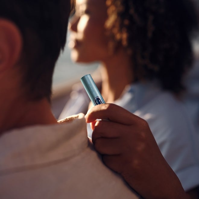 Mujer apoyando la mano con un holder de IQOS ILUMA i en la espalda de un hombre