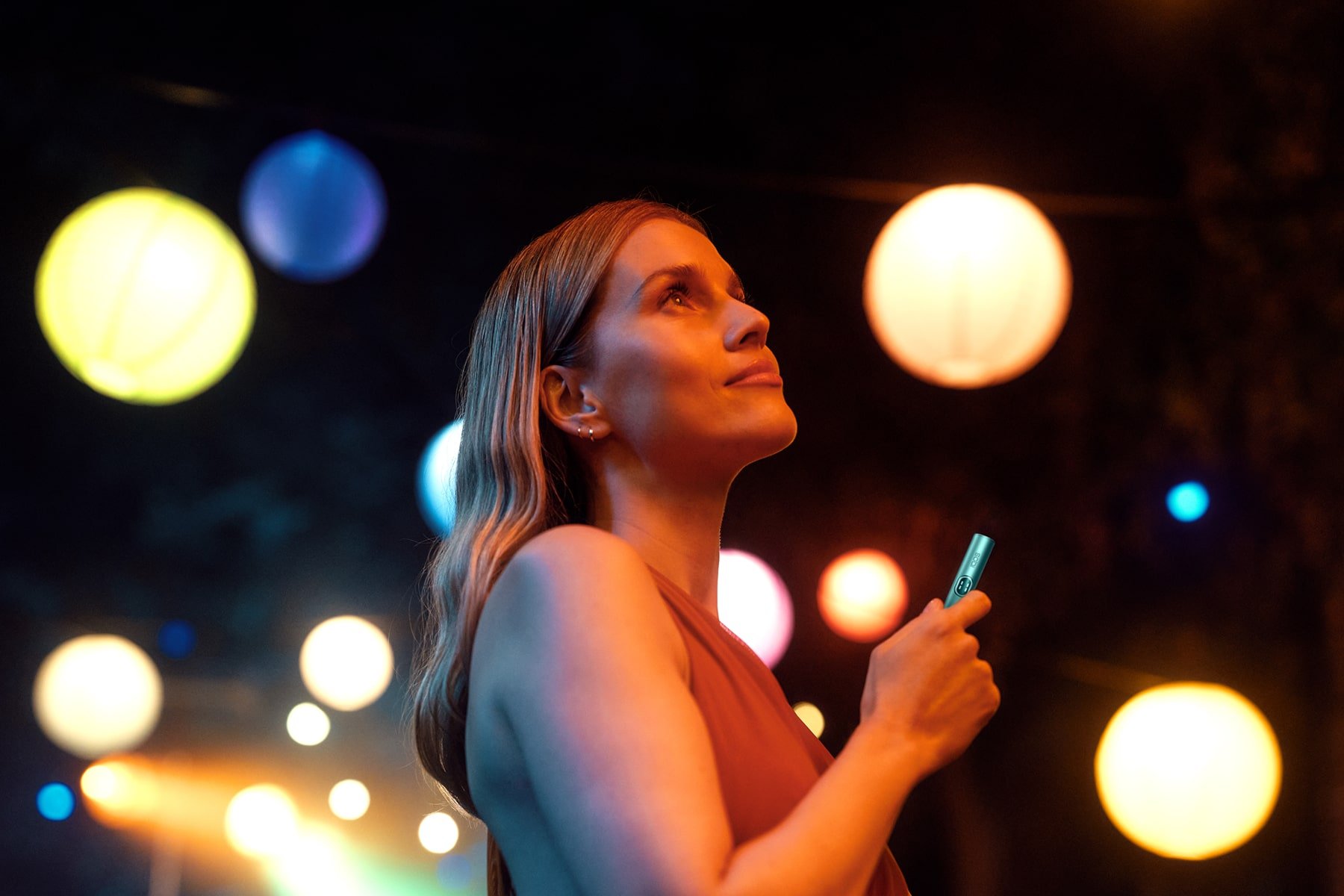 Mujer con holder de IQOS ILUMA i y en el fondo luces de colores