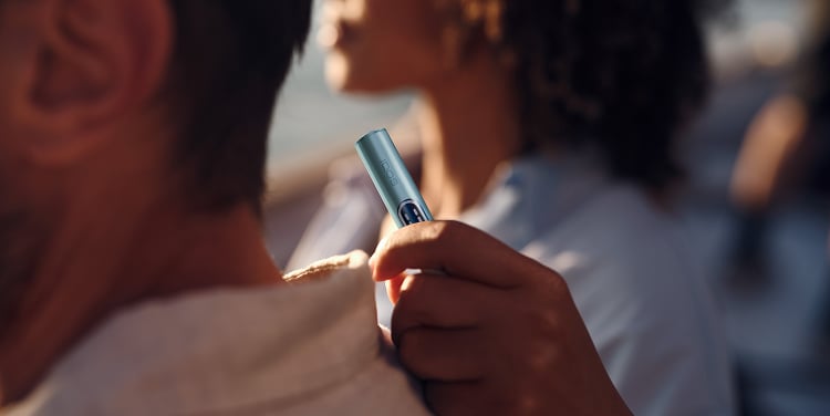Mujer sujetando un IQOS ILUMA i apoyada en el hombro de un hombre