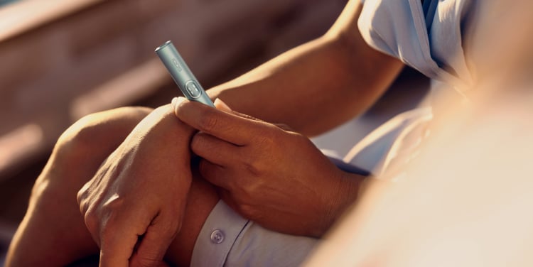 Mujer sujetando un IQOS ILUMA i apoyada en su rodilla