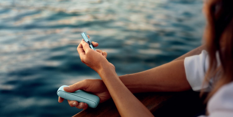 Mujer sujetando un IQOS ILUMA i con el mar de fondo