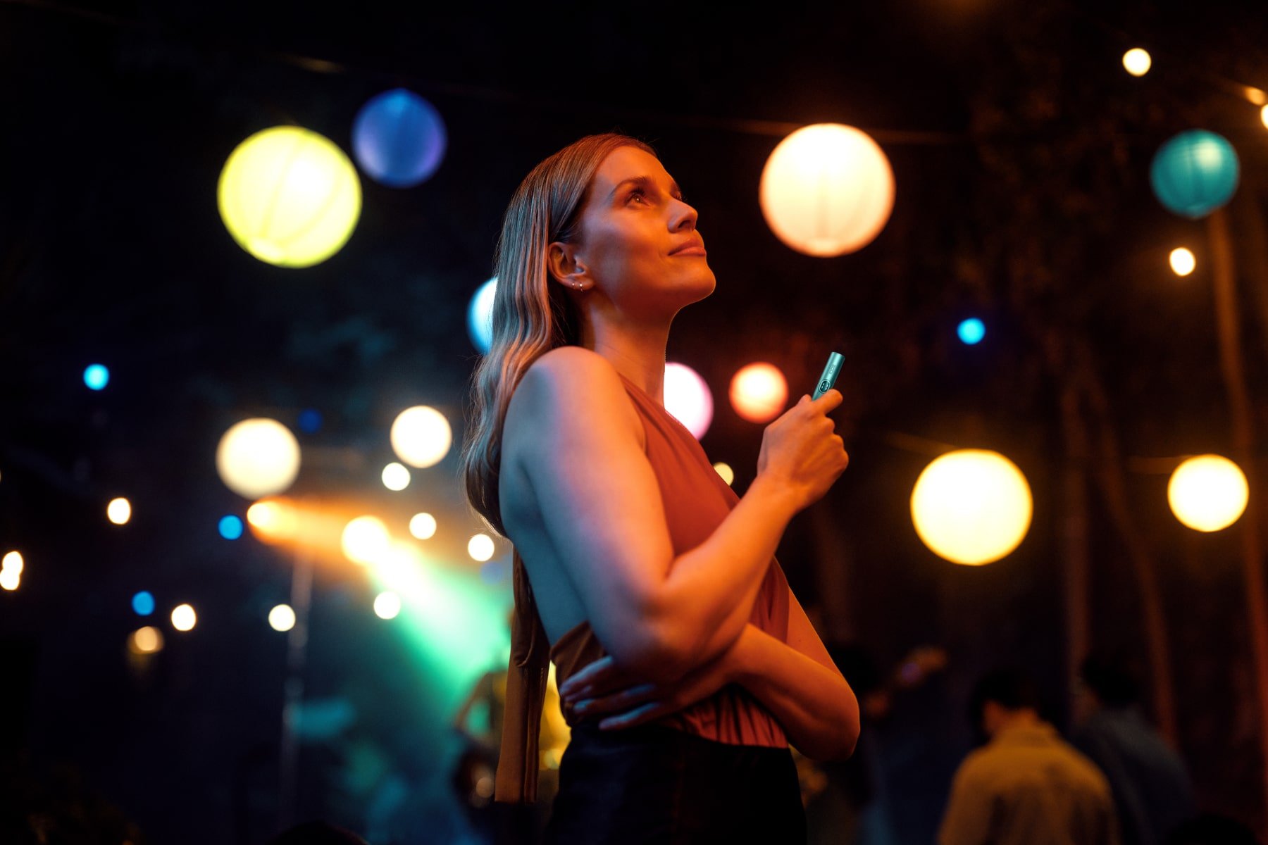 Chica con IQOS ILUMA i y luces de fondo