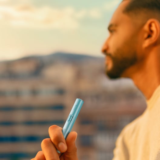 Hombre mirando el horizonte mientras sostiene un dispositivo IQOS azul