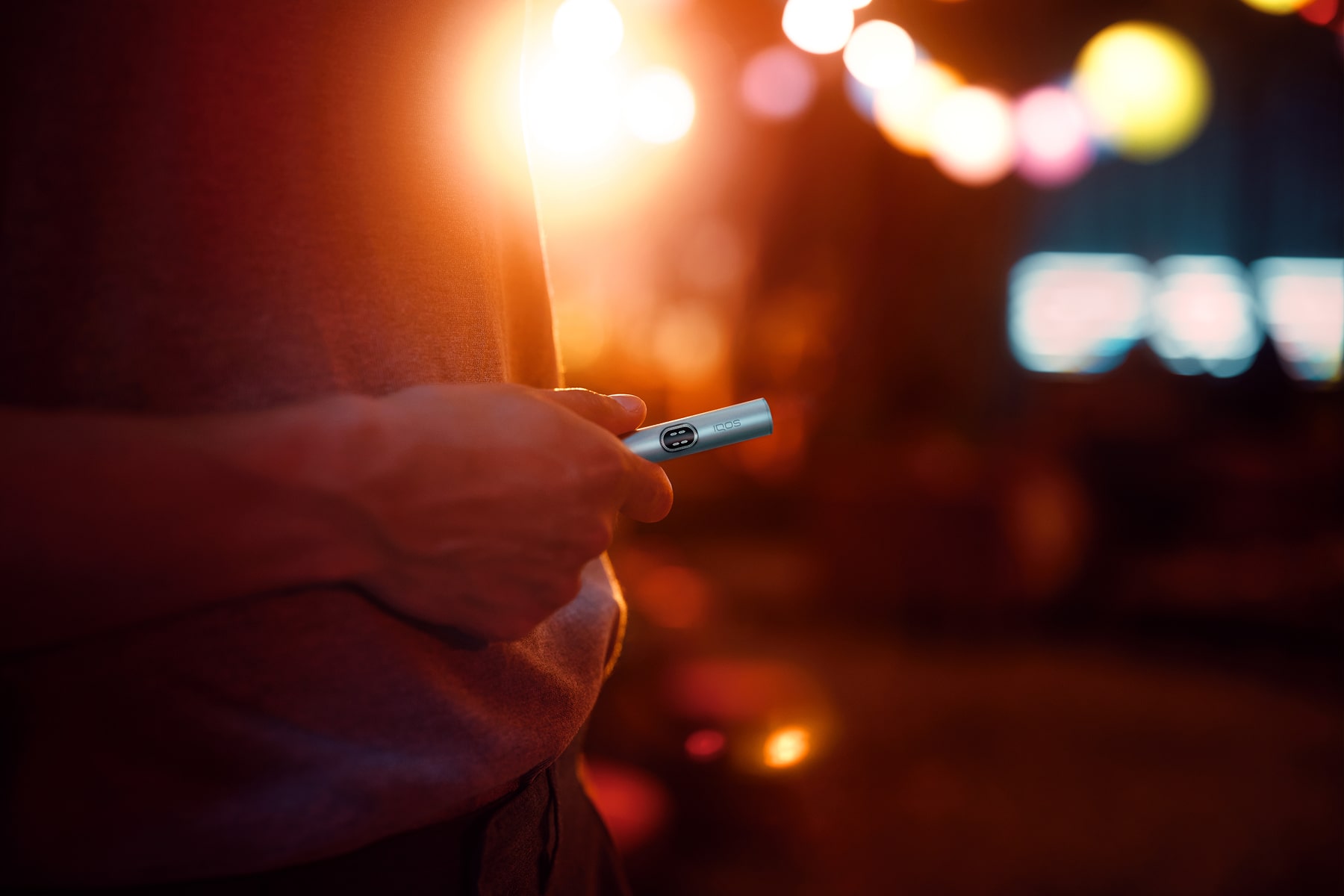 Hombre sujetando el holder de IQOS ILUMA i en Azul brisa y luces de colores en el fondo