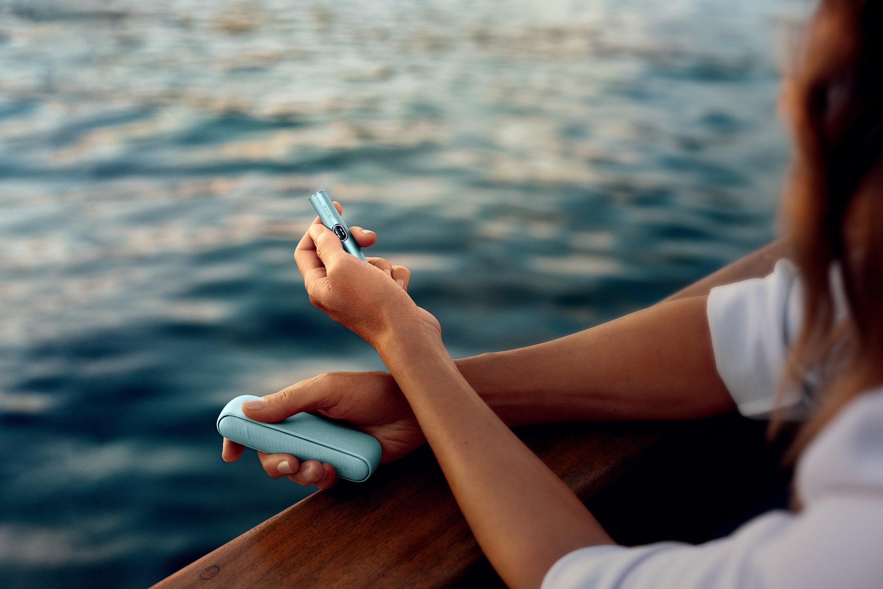 Mujer con IQOS ILUMA i en la mano y el mar de fondo