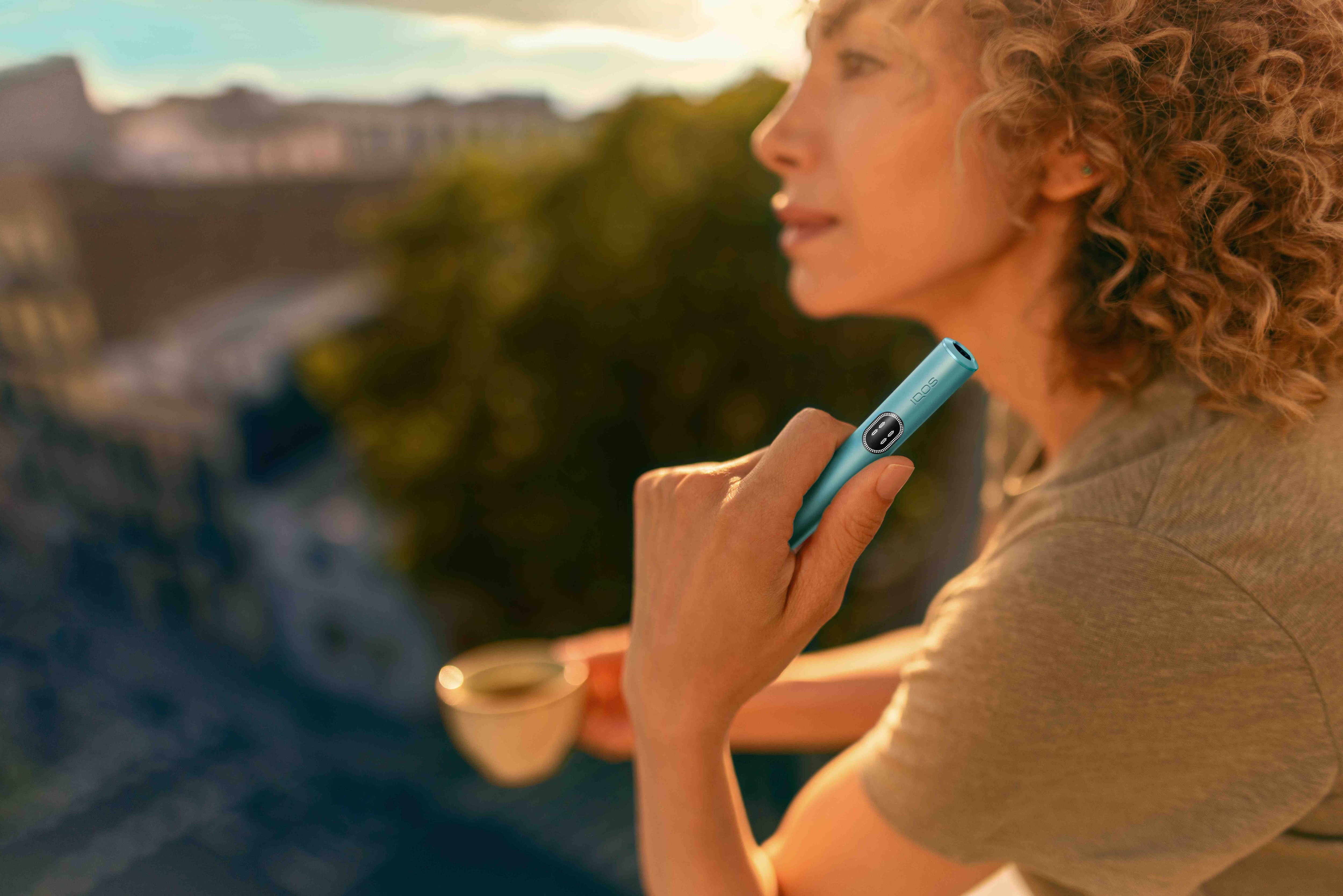 Mujer sujetando un iqos en una terraza