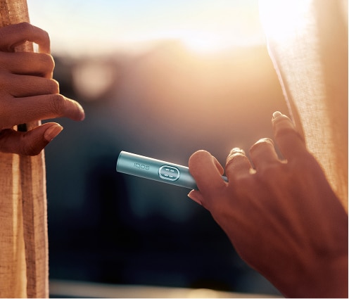Usuario de IQOS asomándose a la ventana con su dispositivo IQOS ILUMA i