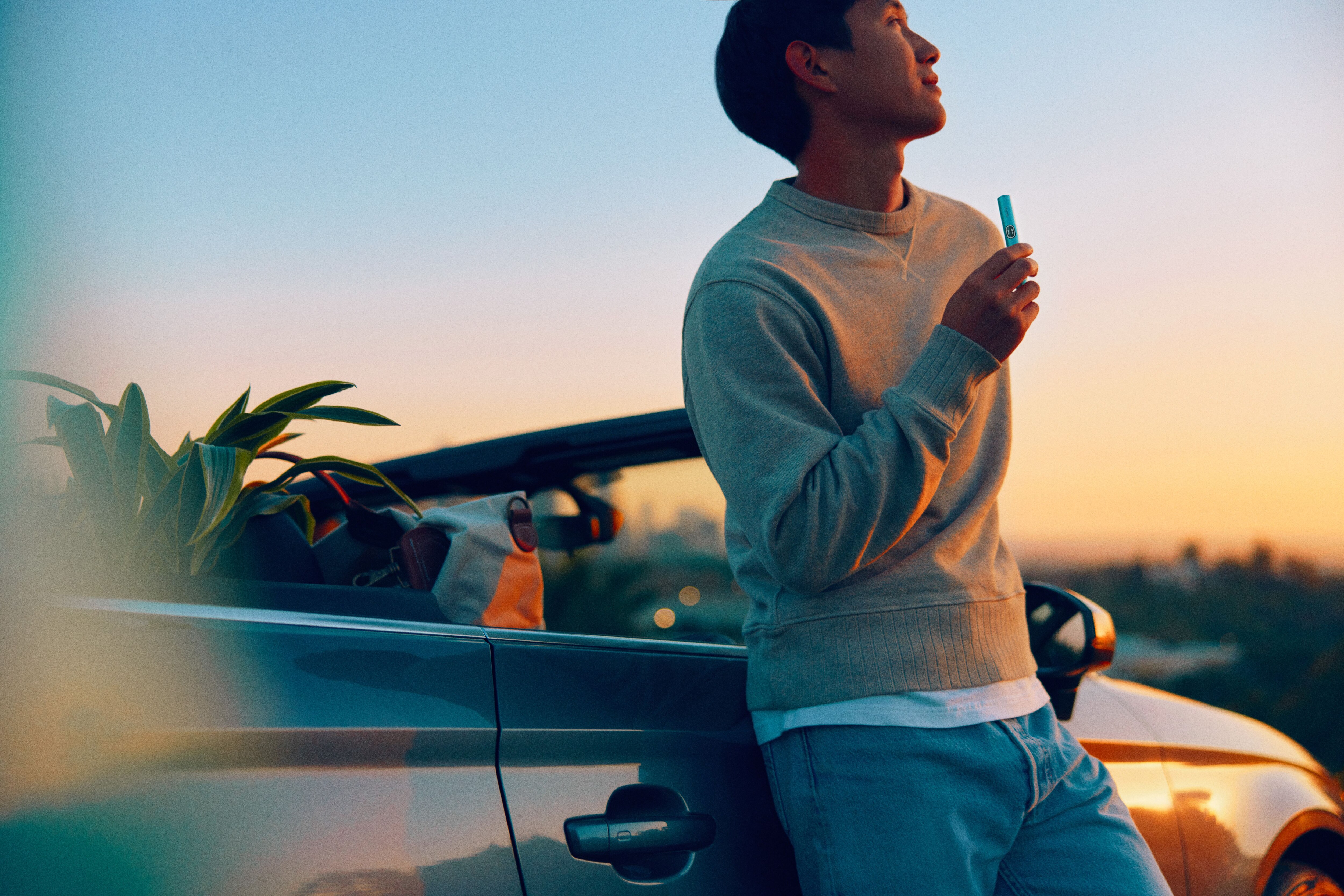 Hombre fuera de su coche con atardecer y un IQOS