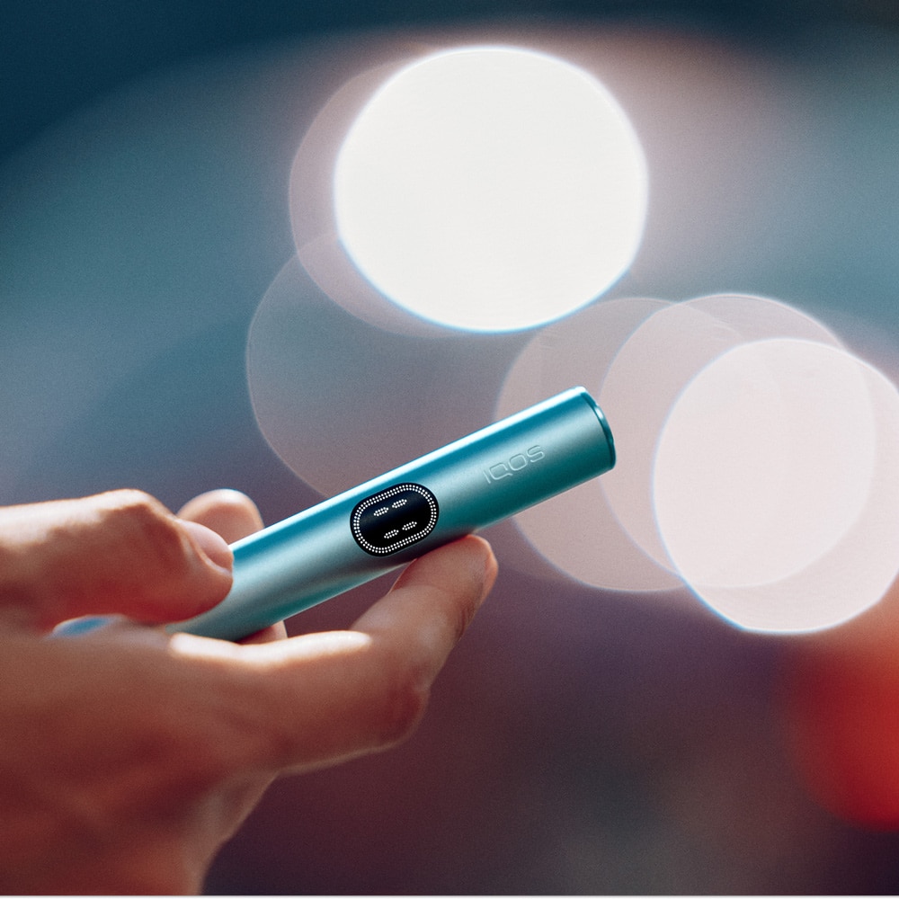Primer plano de una mano sujetando un dispositivo electrónico azul turquesa con pantalla circular iluminada.