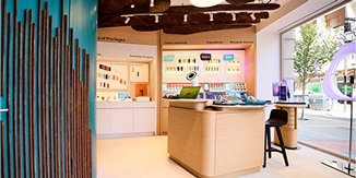 Interior de una tienda IQOS con mostrador central, taburete y expositores iluminados
