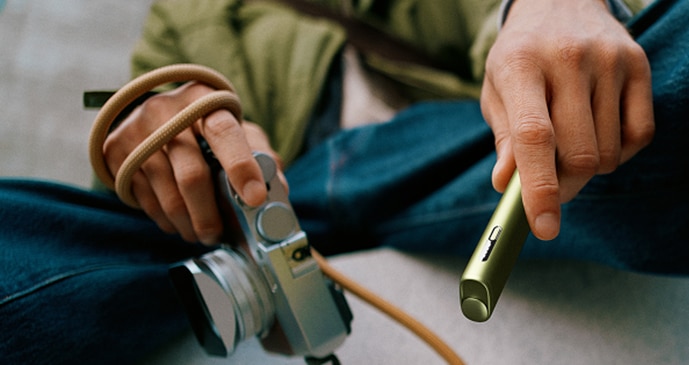 Persona sentada con vaqueros sosteniendo un dispositivo IQOS verde