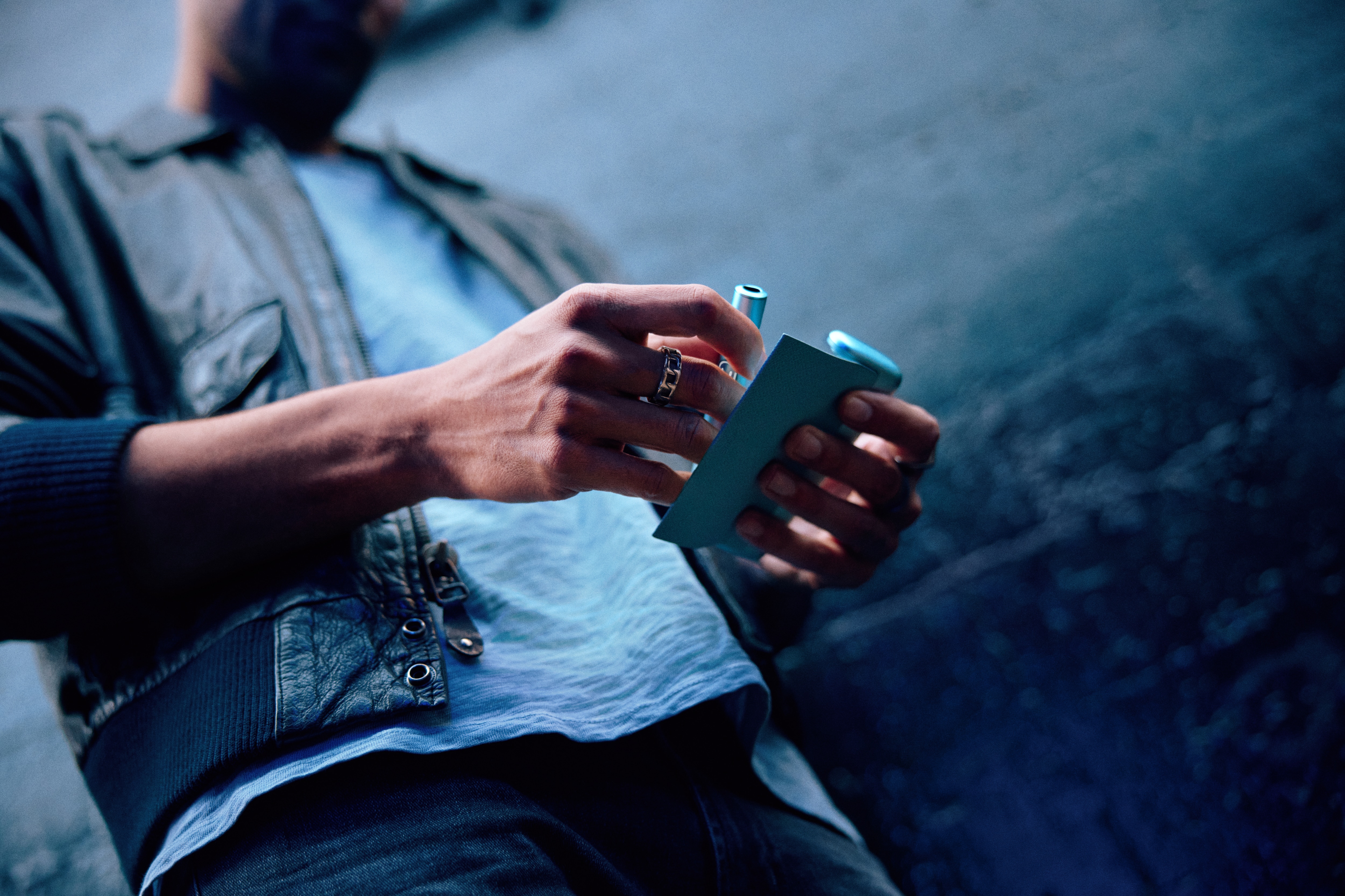 Hombre con un fondo oscuro sujetando un IQOS azul