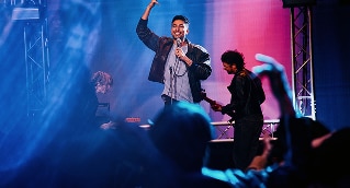 Cantante y público de espaldas, en escenario con luces azules y rosas