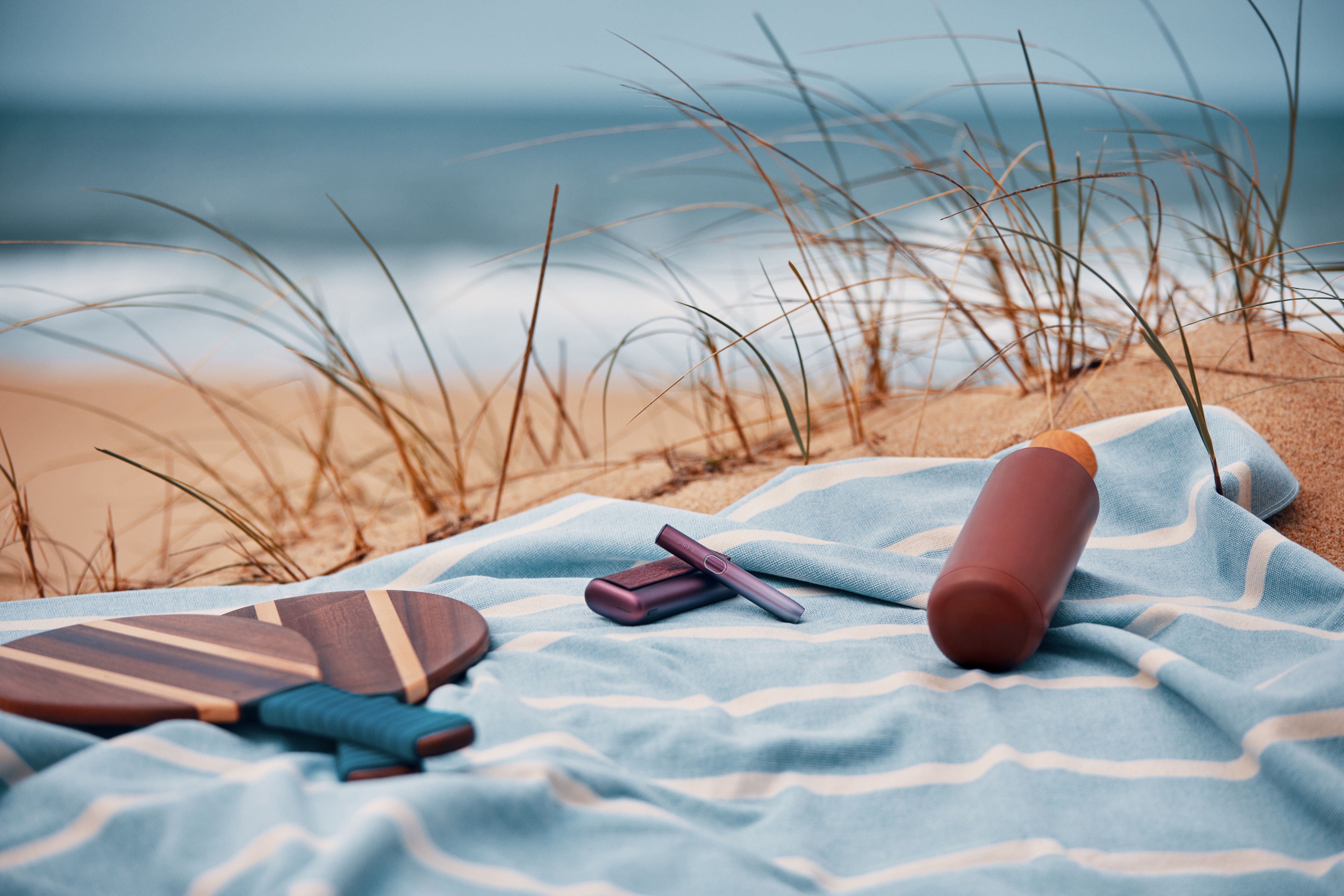 Dispositivos IQOS sobre una toalla en la playa