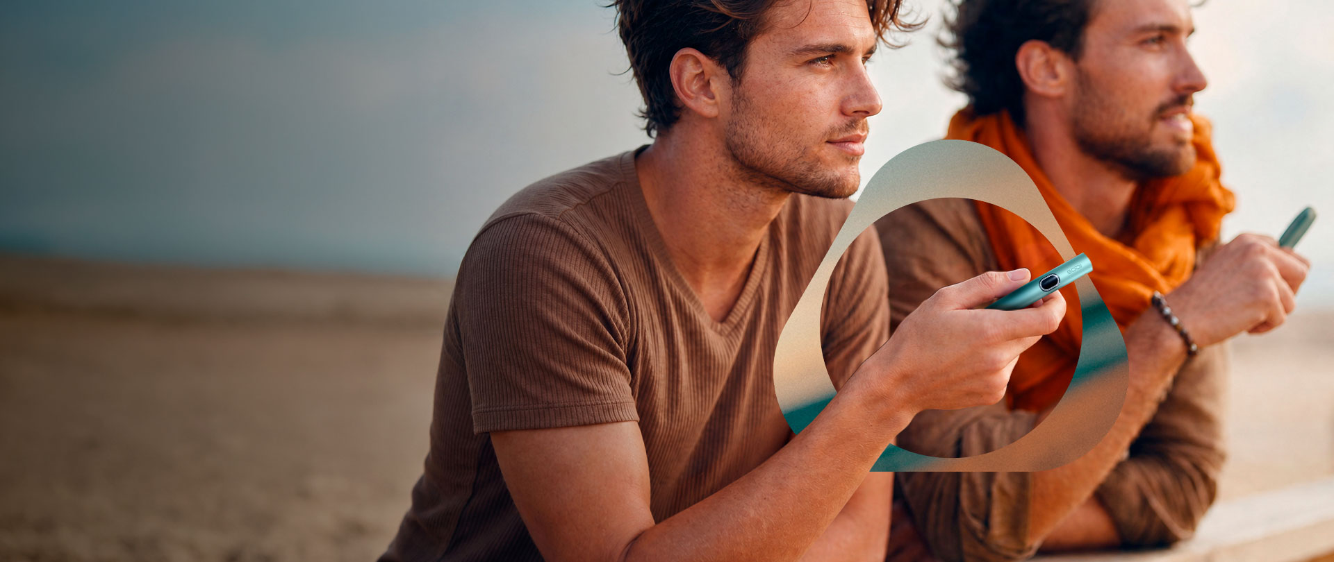 Dos usuarios de IQOS apoyados en una barandilla observando la playa.