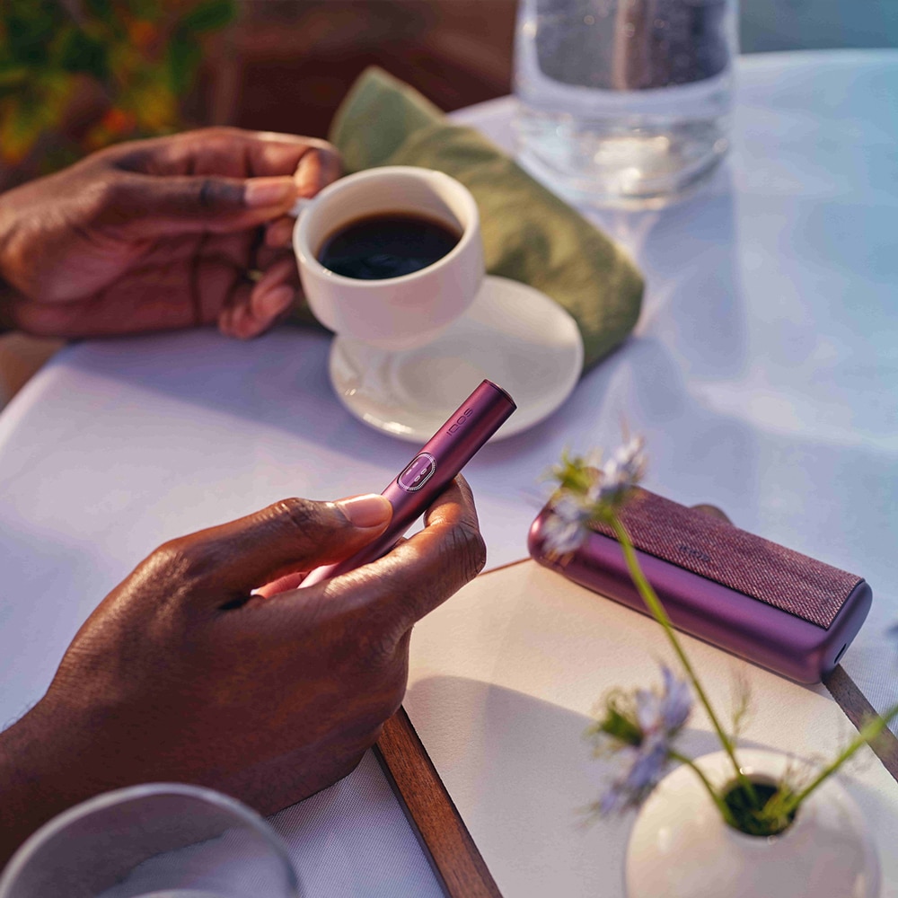 Mujer sujetando un iqos en la mano derecha, y en la izquierda una taza de café.
