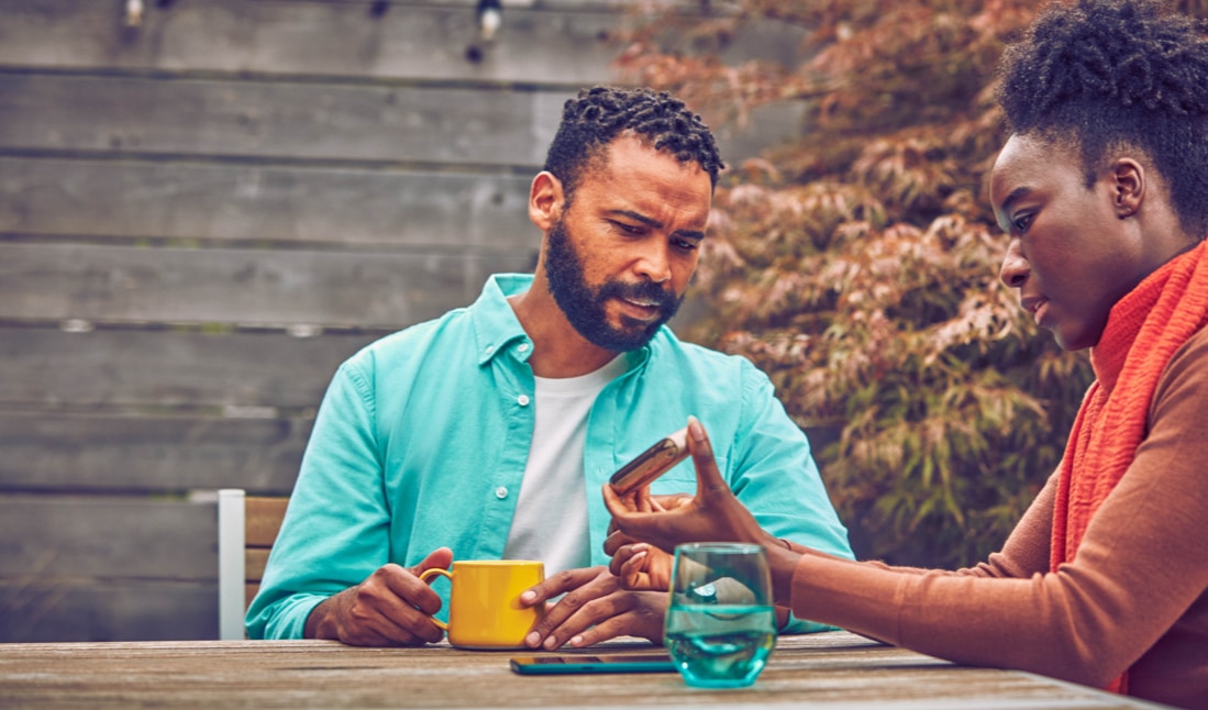 Dos personas hablando en una terraza donde uno de ellos sostiene un dispositivo IQOS Iluma