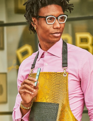 A person holding an IQOS device while standing in front of a barber shop.