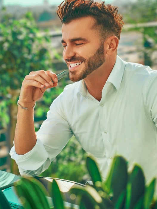 A smiling man holding an IQOS ILUMA device.