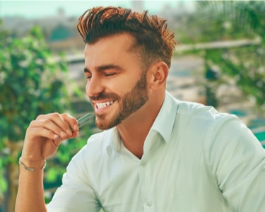 A smiling man holding an IQOS ILUMA device.