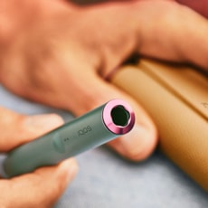 A Jade Green IQOS ILUMA Holder with a ring accessory held by a person with a leather-like full wrap.