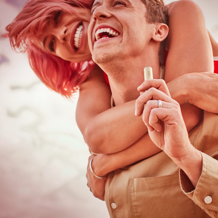 A man holding an IQOS device is embraced by a friend.