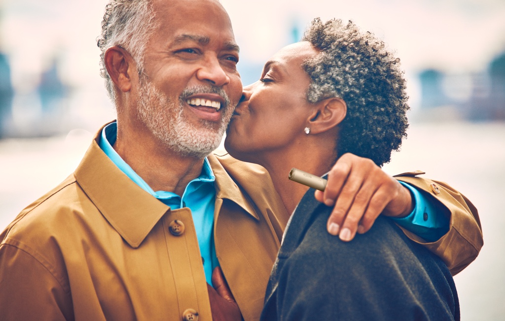 Un hombre sujetando un dispositivo IQOS abraza a su pareja